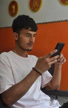 A handsome Indian young guy using his phone while sitting over chair in indoors Foto stock