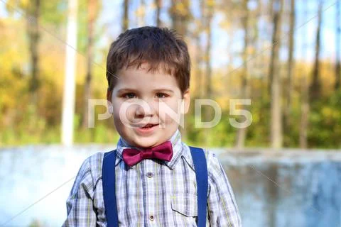 Handsome little plump boy in shirt and bow tie smiles in sunny green park Stock Photos