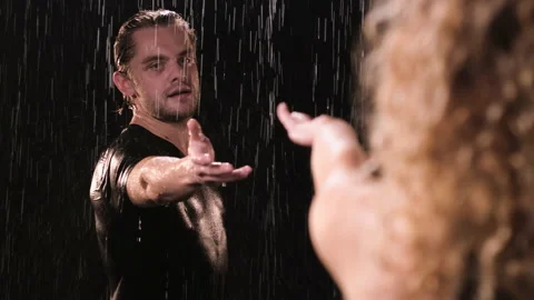 Handsome long haired fair haired guy in black T-shirt stands in the rain and Stock Footage 139723401