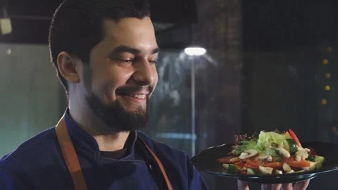 Handsome male chef smiling while holding a vibrant plate of fresh salad Stock Footage 311944770