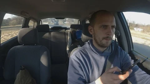 Handsome male driver uses a smartphone while driving a car. Stock Footage 106930095