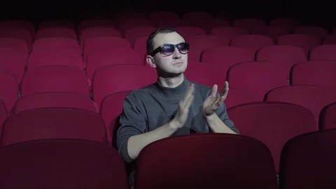 Handsome man in 3d glasses sitting in comfortable red chairs in dark cinema Stock Footage 83950448