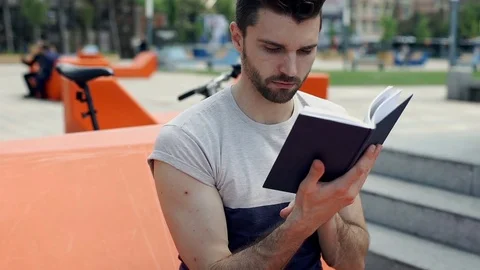Handsome man answers cellphone while reading book in the city, steadycam shot Stock-Footage 77035760