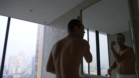 A handsome man applying a razor in the bathroom with a view from the window to Stock Footage 86701516