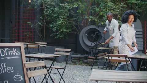 Handsome man arranging chairs down on floor while cute woman wiping tables Stock Footage 254677906