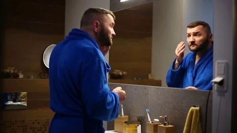 Handsome man in bathrobe checking his appearance in the mirror and drink caffee Video stock 73753888