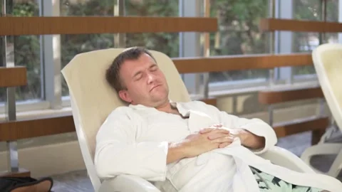 A handsome man in a bathrobe sleeps on a sun lounger by the hotel's pool Stock Footage 233062148