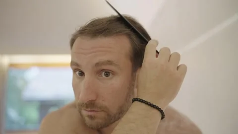 Handsome man with a beard combing his hair while looking at his reflection in Stock Footage 335268252