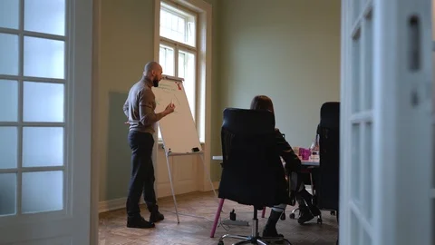 Handsome man with beard discusses strategy with a team, draws on a flipchart 스톡 동영상 124717297