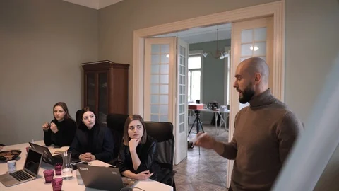 Handsome man with beard discusses strategy with a team, draws on a flipchart 스톡 동영상 124718062
