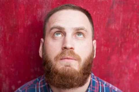 Handsome man with beard on red background looking up Foto stock