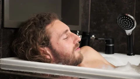 A handsome man with a beard takes a bath with foam looks at the camera. Stock-Footage 167219586