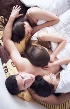 Handsome man in bed with three beautiful woman young macho playboy handsom... Stock Photos