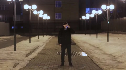 Handsome man in a black coat talking on a smartphone at night Video stock 152983418