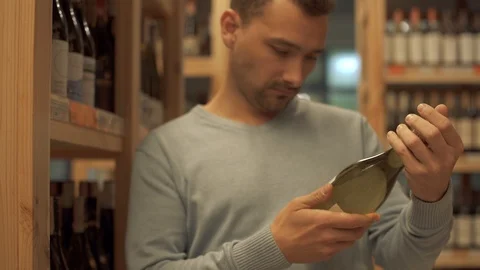 Handsome man carefully examines the composition on the label of a white wine Video stock 99386045