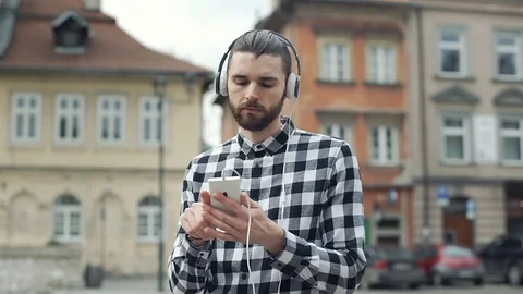 Handsome man in checked shirt standing in the old town and listening music Video stock 73408911