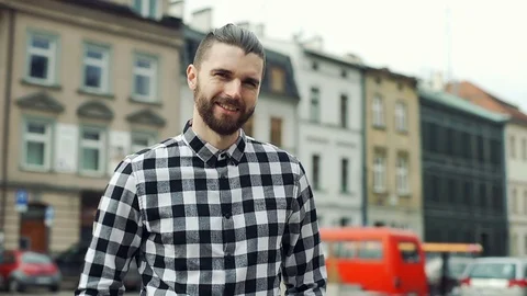 Handsome man in checked shirt standing on the square in old town and smiling  Video stock 73412852