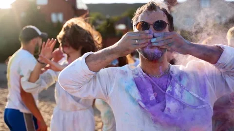 Handsome man claps hands with colored powder in and paints his moustache with Stock-Footage 172424674