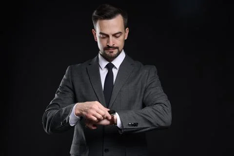 Handsome man in classic suit checking time on black background Stock Photos