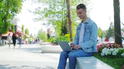 Handsome man in denim jacket sits on parapet with notebook 스톡 동영상 112124479