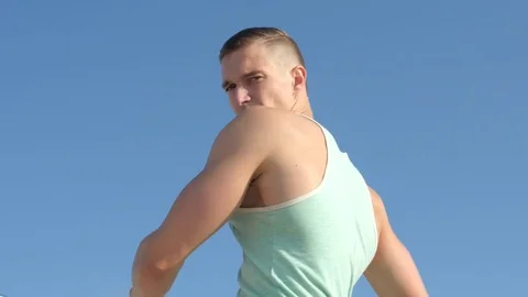 Handsome man does morning exercise on the beach outdoors against blue sky. 4k Stock Footage 84041411
