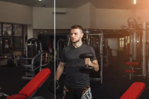 Handsome man doing biceps lifting with dumbbell on bench in a gym Stock Photos