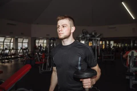 Handsome man doing biceps lifting with dumbbell on bench in a gym Stock Photos