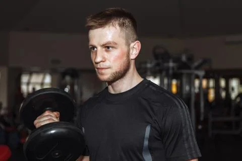 Handsome man doing biceps lifting with dumbbell on bench in a gym Stock Photos