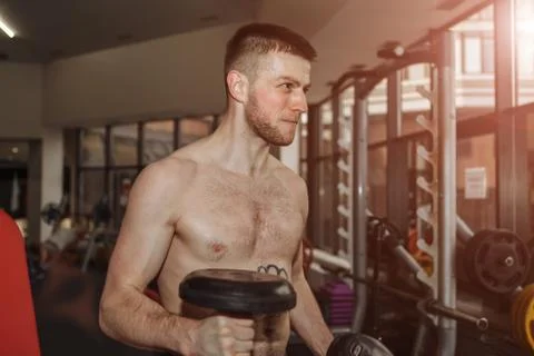 Handsome man doing biceps lifting with dumbbell on bench in a gym Stock Photos