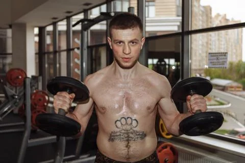 Handsome man doing biceps lifting with dumbbell on bench in a gym Foto stock