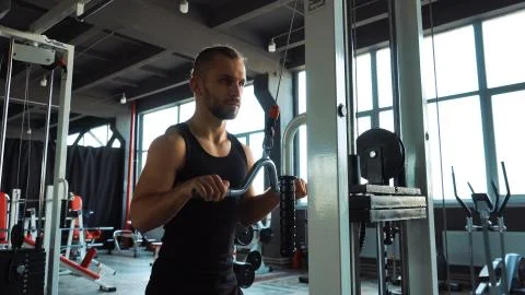 Handsome man doing exercise in the simulator with one hand in fitness gym Stock Photos