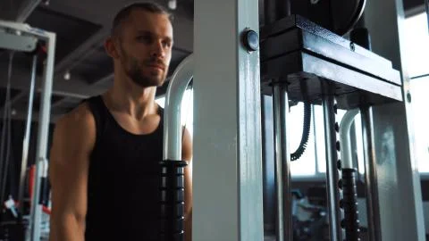 Handsome man doing exercise in the simulator with one hand in fitness gym Stock Photos