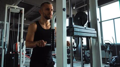 Handsome man doing exercise in the simulator with one hand in fitness gym Stockfoto's