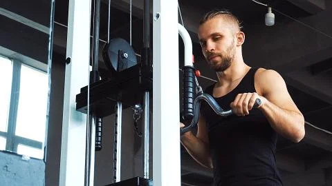 Handsome man doing exercise in the simulator with one hand in fitness gym Stock Photos