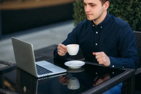 Handsome man drink cappuchino in cafe on the terrace and look into his laptop Stock Photos