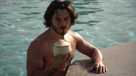 Handsome man drinking coconut juice in swimming pool at clubhouse in hotel. Stock Footage 147424912