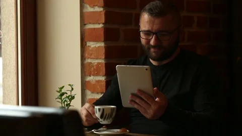 Handsome man drinking coffee in the cafe and watching something on tablet Stock Footage 80423131