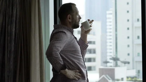 Handsome man drinking coffee in his room and admires the view from window  Stock Footage 88436085