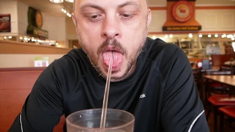 Handsome man drinking cold water from the glass with a straw in a restaurant Stock Footage 77632519
