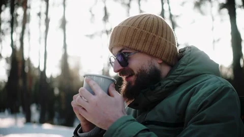 Handsome man drinking hot drink in the woods in winter, enjoying camp life Video stock 169503545
