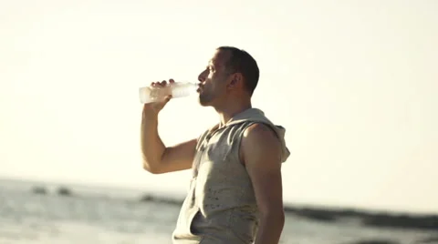Handsome man drinking water on the beach, slow motion, shot at 240fps HD Vídeo Stock 56978931