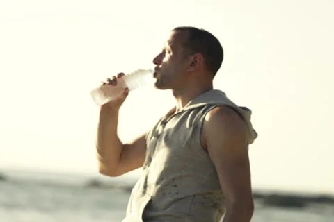 Handsome man drinking water on the beach, slow motion, shot at 240fps NTSC Stock-Footage 56978937