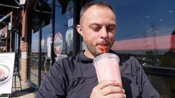 Handsome man drinks smoothie with a straw sitting outside the cafe store Stock Footage 85675387