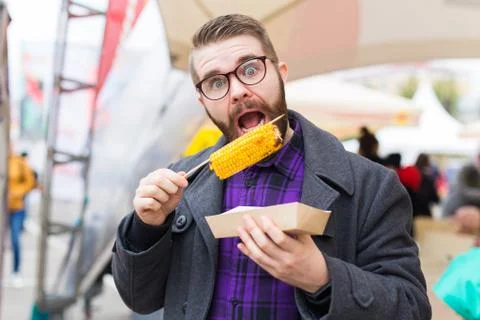 Handsome man eating roasted corn on the street. Stock Photos