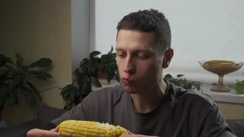 Handsome man eats a corn cob in his kitchen at home Stock Footage 316404671