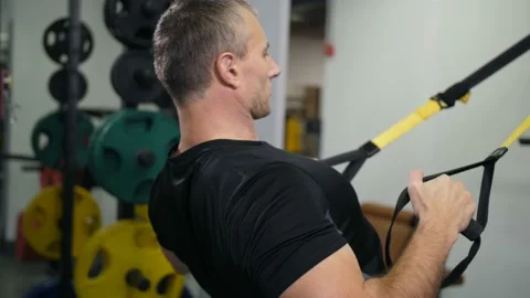 Handsome man is engaged on TRX. Makes an exercise for the arms and back 4K Slow Видео 100257802