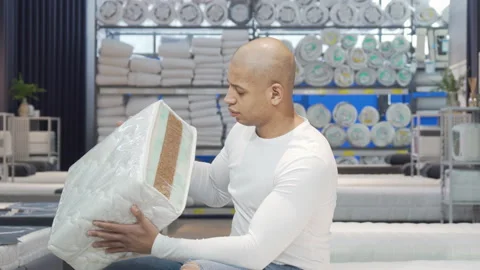 Handsome man examining sample of orthopedic mattress on sale Stock Footage 148346524