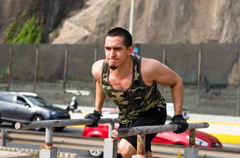 Handsome man exercising on parallel bars on the street outdoors. Stock Photos
