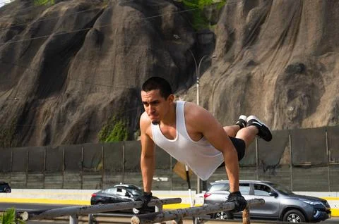 Handsome man exercising on parallel bars on the street outdoors. Stock Photos
