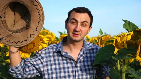 Handsome man farmer putting hat off welcoming someone at camera in sunflowers Stock Footage 138400244
